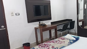 A bedroom with a bed, a desk with a chair, a television mounted on the wall, and a mirror. - The Lemon House (Guwahati)