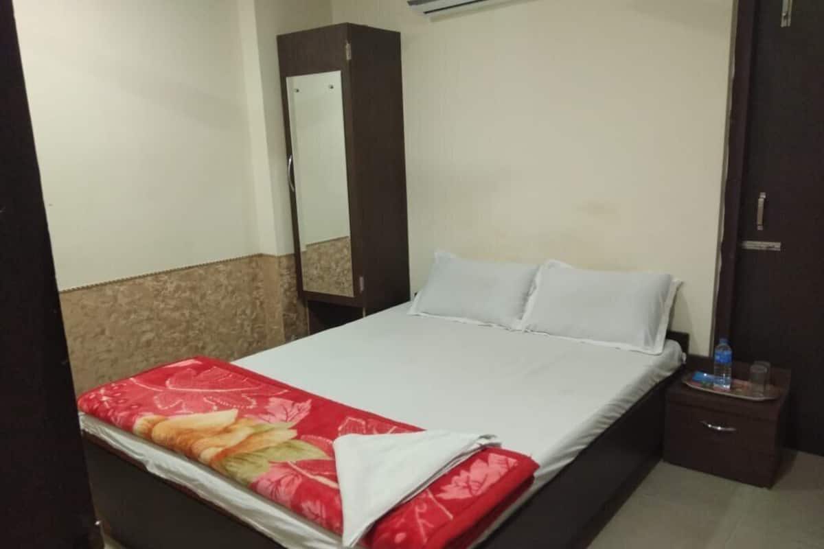 A neatly made bed with a red floral bedspread, a white pillow, and a wooden nightstand with a water bottle and glass.