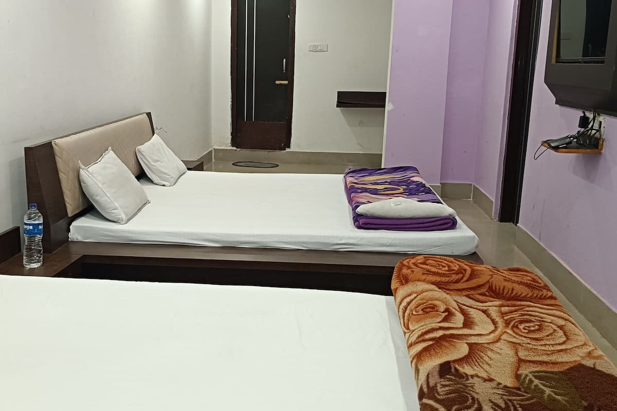 A hotel room with two beds, a television mounted on the wall, and a water bottle on the nightstand.