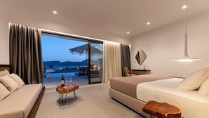 Une chambre d’hôtel moderne dotée d’une grande porte-fenêtre coulissante donnant sur un espace piscine, d’un canapé, d’une table basse en bois et d’un luminaire suspendu.