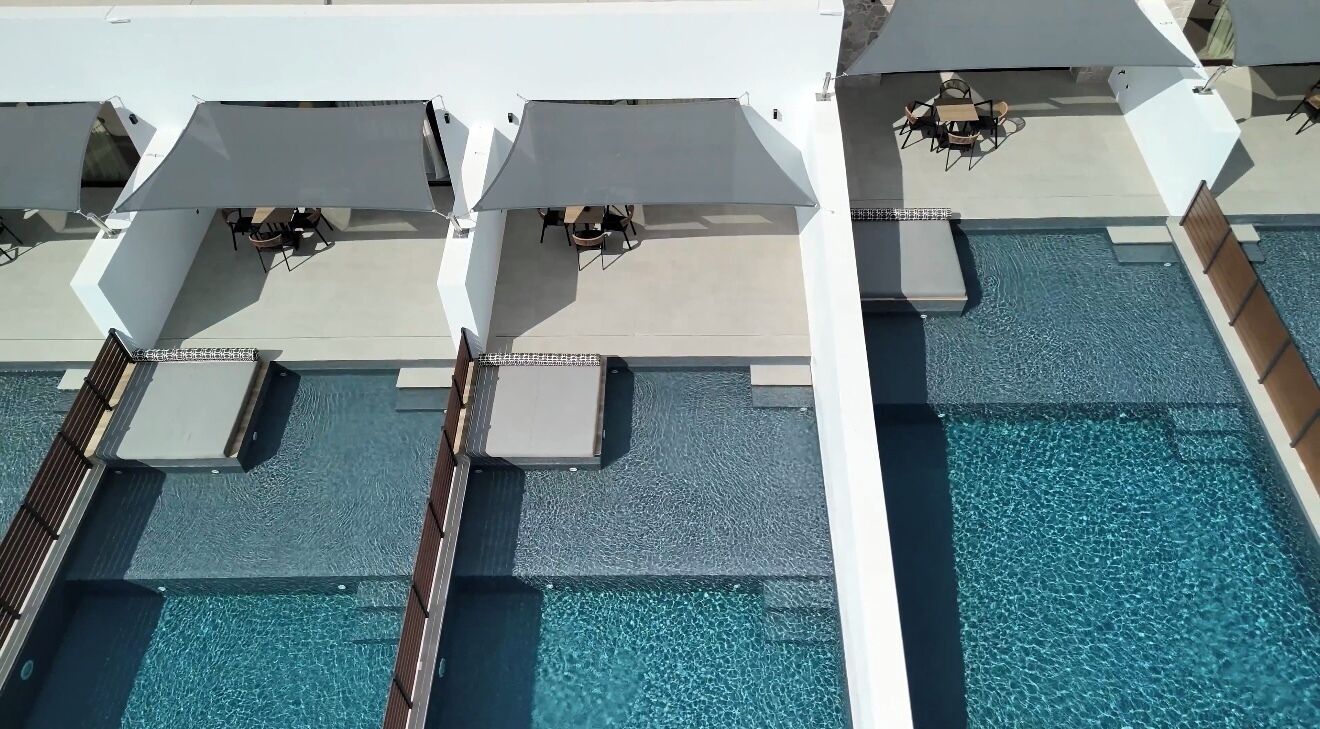 A rooftop pool area with multiple sun loungers and umbrellas, a clear blue pool, and a view of the surrounding architecture.