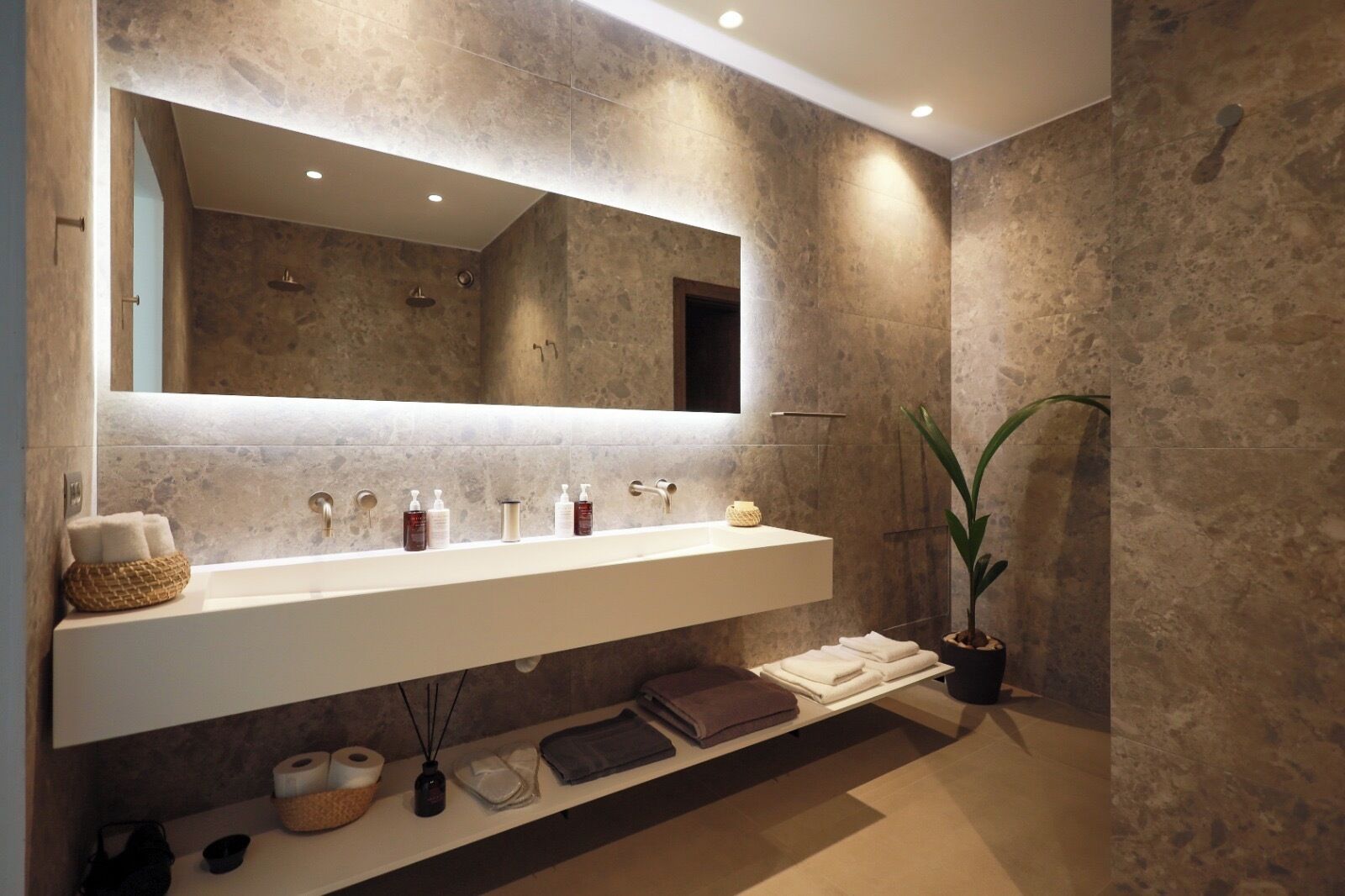 A modern bathroom with a large mirror, a white vanity, and a potted plant.