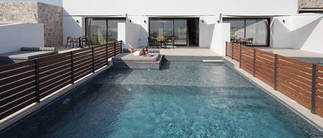 A rooftop pool with clear blue water, surrounded by modern outdoor seating and a stone wall.