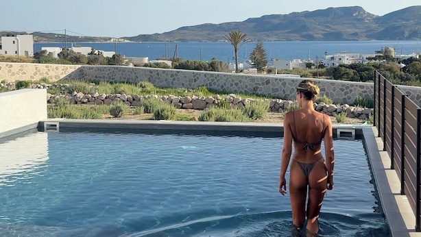 Une personne se promène dans une piscine d’où l’on peut admirer la mer et les montagnes.