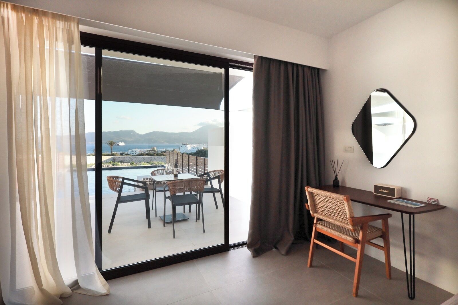 A modern hotel room with a balcony, a dining table, and a desk.