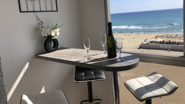 A balcony with a table, two chairs, a bottle of wine, and a vase of flowers.