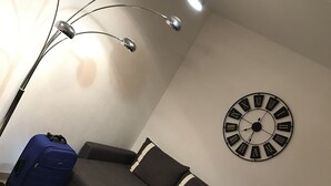 A living room with a sectional sofa, a blue suitcase, a floor lamp, and a wall clock.