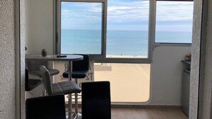 A room with a view of the beach, a table with chairs, and a small shelf with a can.