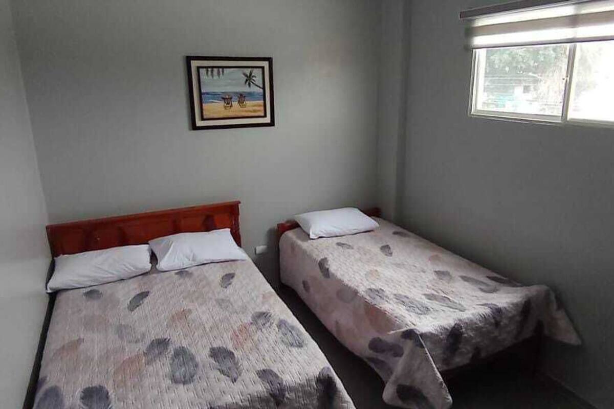Quarto pequeno com duas camas de solteiro, televisão, quadro na parede e janela.