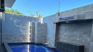 Una piscina rectangular con superficie de agua azul cristalina, rodeada de muros de piedra gris y una terraza con baldosas.