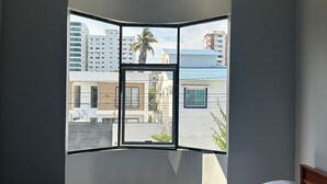Un dormitorio con ventanal curvo, una cama y vistas a edificios y una palmera al exterior.