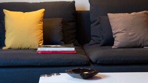 A dark-colored sofa with two cushions, one yellow and one brown, and a small table with a book and a tray. - Stylish 2 bedroom Apt in Thiseion, large balcony (Athina)