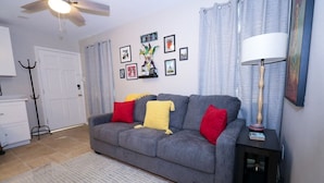 A living room with a grey sofa, red and yellow cushions, a black side table with a lamp, and framed pictures on the wall. - Location, Location, Location! Welcome to a charming 1BR in Uptown New Orleans.  (New Orleans)