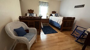 Un dormitorio con una cama de madera, una silla de mimbre blanca, una mecedora azul y un escritorio pequeño.