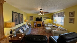 Una sala de estar con un sofá, dos sillones, una mesa de centro, una chimenea, un televisor y un ventilador de techo.