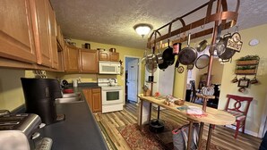 Una cocina con armarios de madera, microondas, estufa, cafetera y un colgador para ollas.