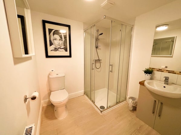 A bathroom with a toilet, a glass-enclosed shower, a sink, and a framed picture on the wall. - Bristol City Stays (Bristol)