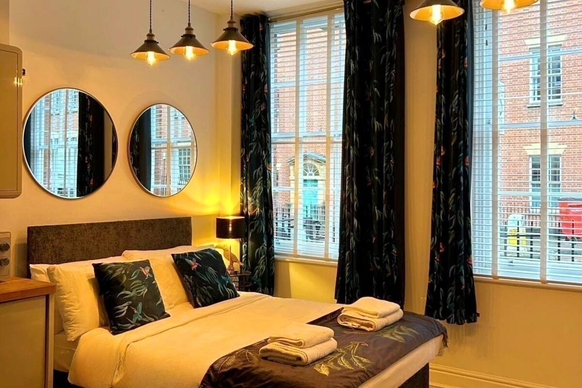 A modern bedroom with a large bed, two round mirrors, and a view of a brick building through the window.