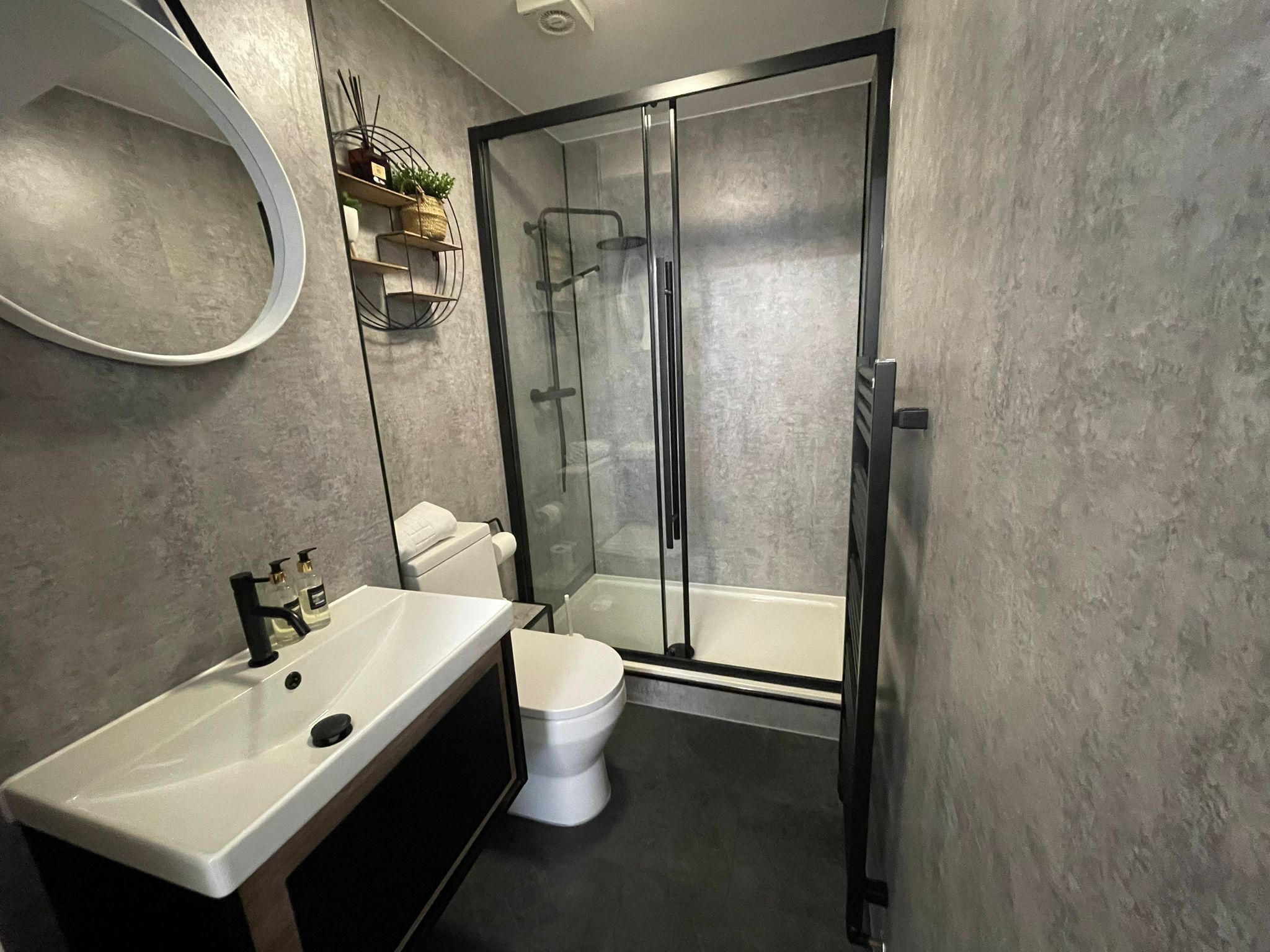 A modern bathroom with a white sink, toilet, and glass-enclosed shower.