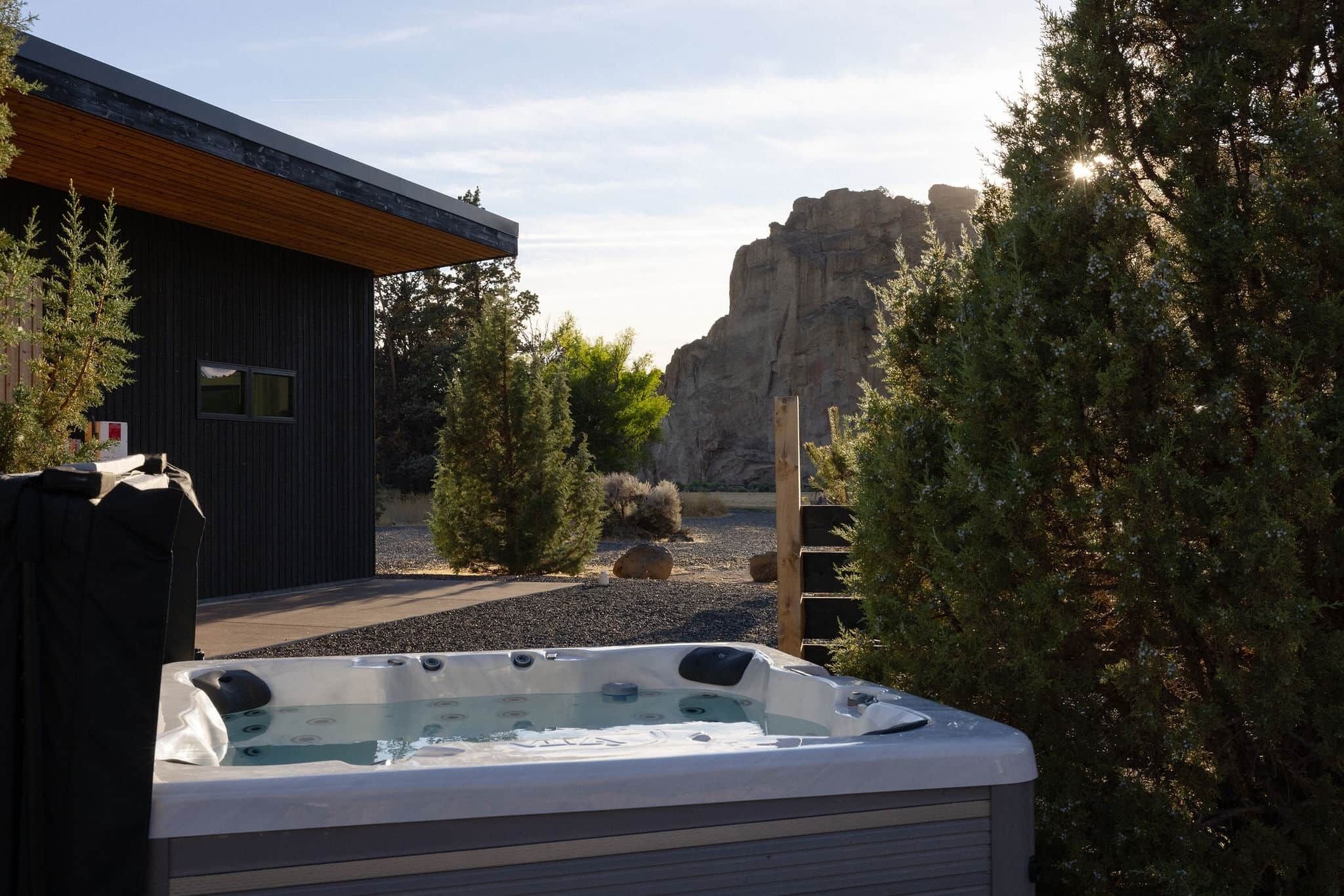 Een modern gebouw met een hottub op de voorgrond, omringd door bomen en een rotsachtig landschap.