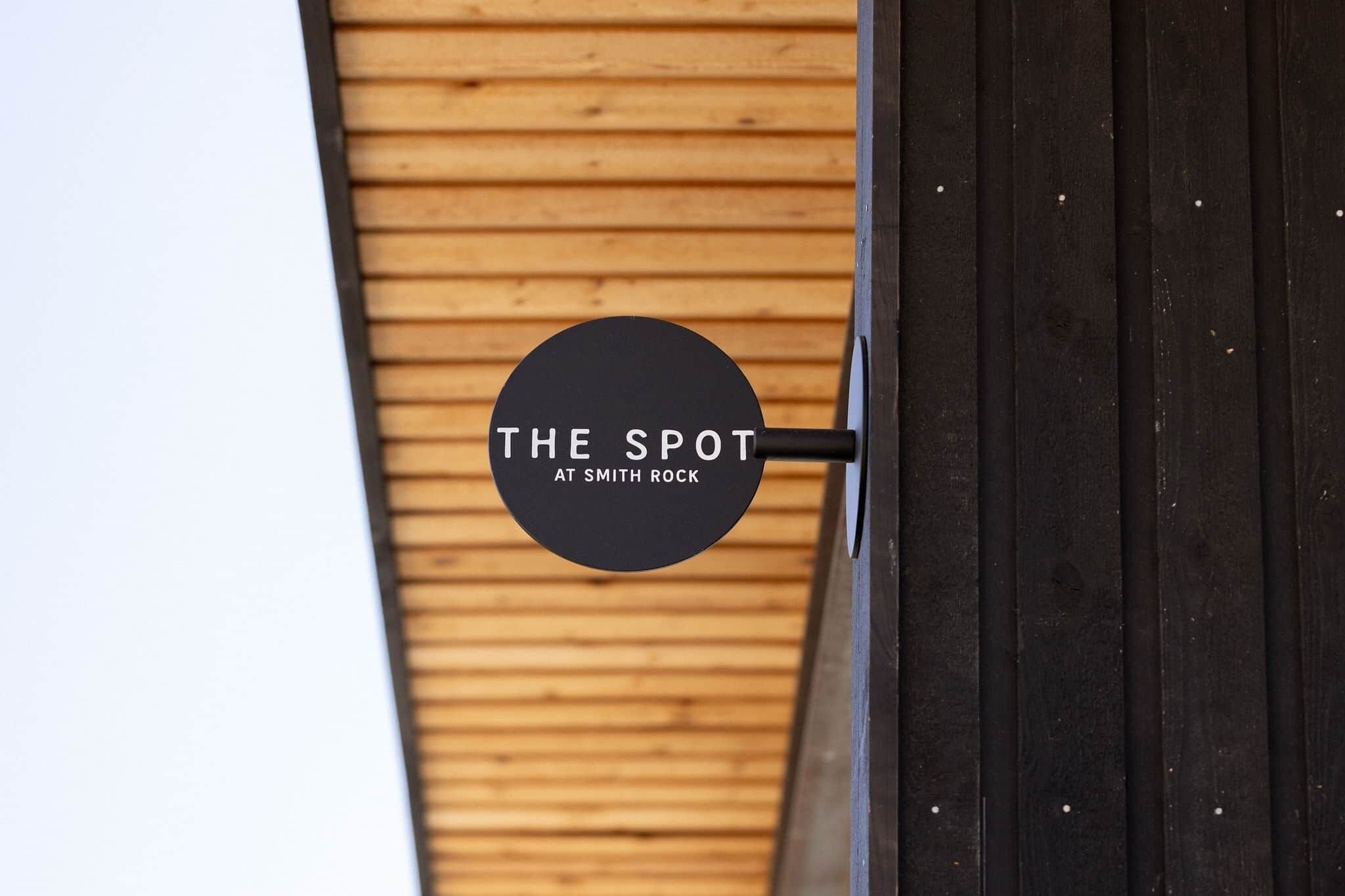 Un letrero circular con el texto 'THE SPOT AT SMITH ROCK' en una pared de madera.