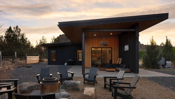 A modern building with an outdoor seating area featuring Adirondack chairs and a fire pit.