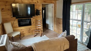 Een houten hut binnen met een aan de muur bevestigde televisie, een bank, een stoel en een ladder.