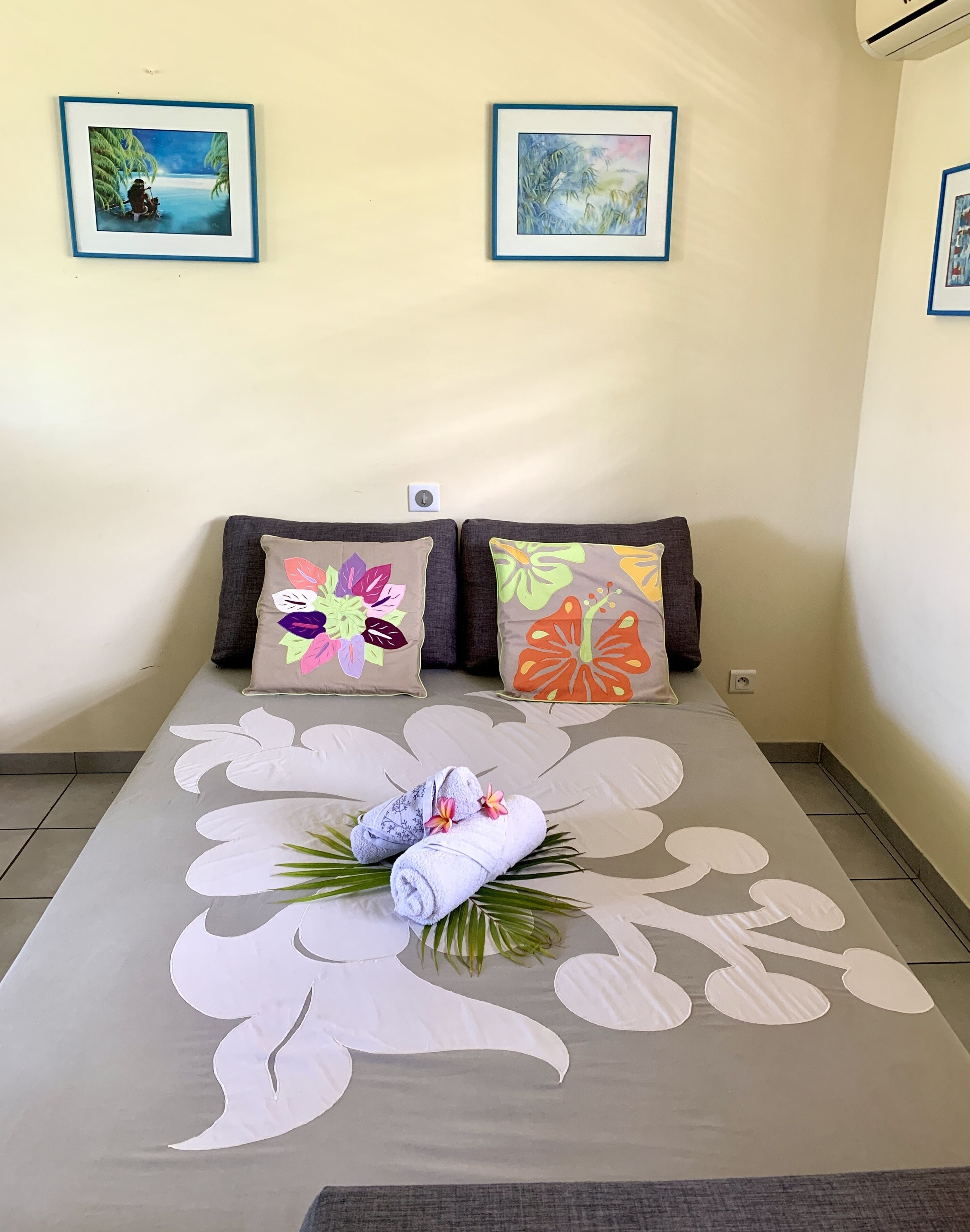 A neatly made bed with floral-patterned bedding, two pillows with colorful floral designs, and a pair of towels with flowers.