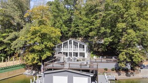 A waterfront property with a two-story house, a dock, and a small boat. - Stunning Lakefront Home in peaceful cove on Lake Lure! (Lake Lure)