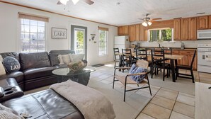 A spacious living room with a leather sofa, a dining area with wooden chairs, a kitchen with wooden cabinets, and ceiling fans. - Stunning Lakefront Home in peaceful cove on Lake Lure! (Lake Lure)