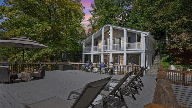 A two-story wooden house with a balcony, outdoor seating, and a stone facade. - Stunning Lakefront Home in peaceful cove on Lake Lure! (Lake Lure)