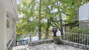 A stone patio with a railing, a welcome sign held by a bear statue, and a view of a body of water and buildings in the background. - Stunning Lakefront Home in peaceful cove on Lake Lure! (Lake Lure)