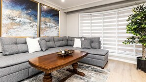 Ein modernes Wohnzimmer mit einem Ecksofa, einem Holztisch und zwei großen abstrakten Gemälden.