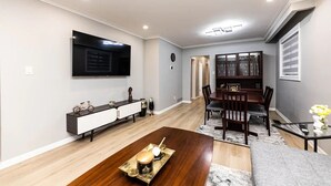 Ein modernes Wohnzimmer mit Flachbildfernseher, einem Esstisch aus dunklem Holz und einem Couchtisch mit einer Dekoration.