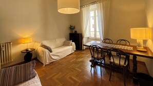 Una sala de estar acogedora con un sofá, una mesa de comedor con sillas, una lámpara y una ventana con cortinas.