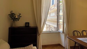 Una habitación con ventana, un aparador de madera oscura, una pequeña mesa con sillas y un florero con flores.