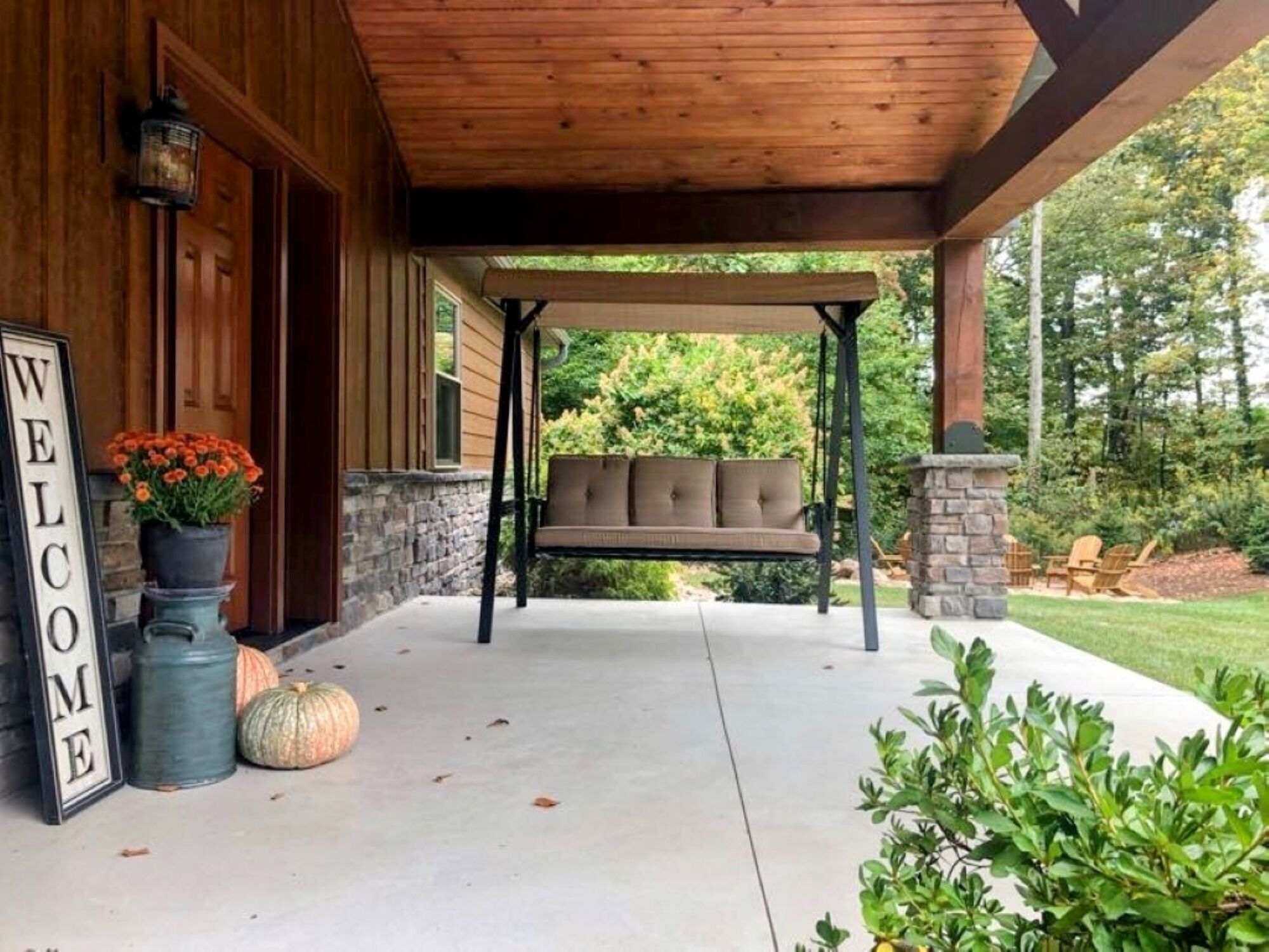 A wooden porch with a swing seat, a welcome sign, and a stone fireplace.