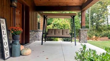 A wooden porch with a swing seat, a welcome sign, and a stone fireplace.