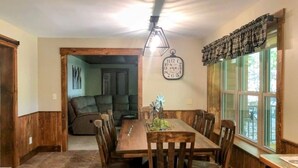 A dining area with a wooden table and chairs, a clock on the wall, and a window with curtains. - Quiet, country home with luxury amenities. (Dundee)