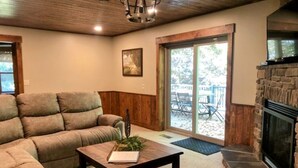 A cozy living room with a sectional sofa, a coffee table with a book and plant, a fireplace, and a sliding glass door leading to an outdoor patio. - Quiet, country home with luxury amenities. (Dundee)