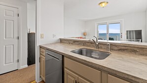 A kitchen with a sink, countertop, and cabinets. There is a window with a view of the sea. - One bedroom, direct ocean views! (Old Orchard Beach)