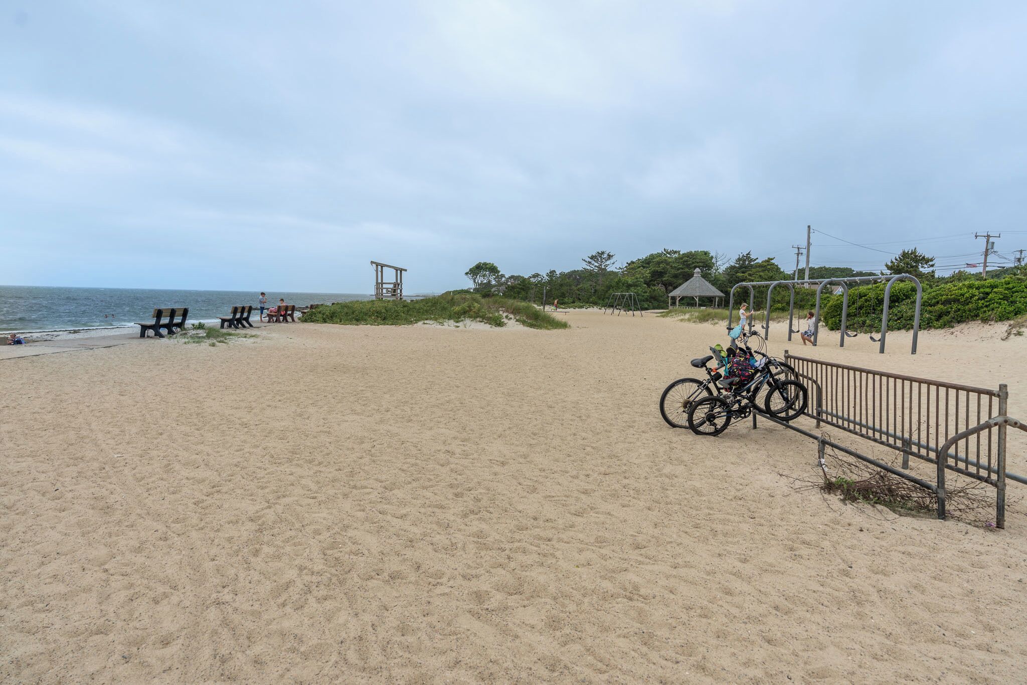 Une plage de sable avec quelques chaises de plage, un vélo et une balançoire.