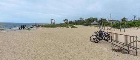 Une plage de sable avec quelques chaises de plage, un vélo et une balançoire.