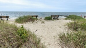 A beach with three wooden benches facing the ocean, surrounded by sand and grass. - Seaside Serenity - New Construction! (Yarmouth)