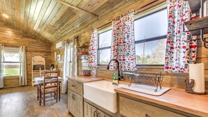 A wooden cabin interior with a kitchen area featuring a sink, wooden cabinets, and a dining table with chairs. - Cozy Mississippi Cabin w/ Covered Porch & Grill! (Glen)