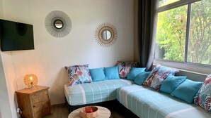 Un salon accueillant avec un canapé d’angle, une petite table d’appoint en bois, une table ronde en bois et un téléviseur fixé au mur.