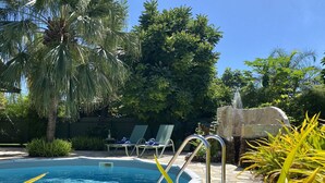 Une piscine avec des chaises longues, un palmier et une fontaine en pierre.