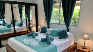 Un lit bien fait, avec une literie et des oreillers de couleur turquoise, une tête de lit en bois, une table de chevet avec une lampe et un grand miroir qui reflète la pièce.