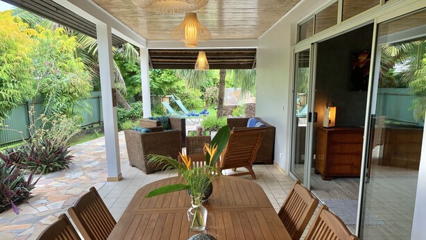 Une terrasse couverte avec une table en bois, des chaises et un vase rempli de fleurs.