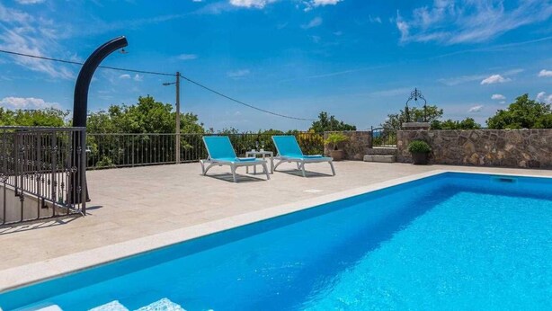 Une piscine avec deux chaises longues, un mur de pierre et un ciel bleu azur.